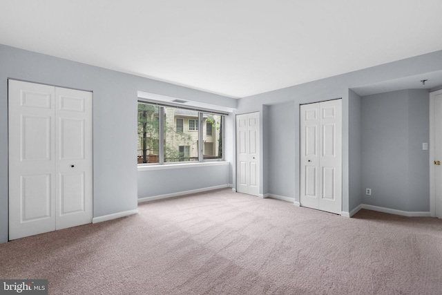 unfurnished bedroom with multiple closets, light colored carpet, and baseboards