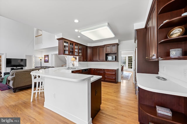 kitchen featuring a peninsula, light countertops, open shelves, stainless steel microwave, and glass insert cabinets