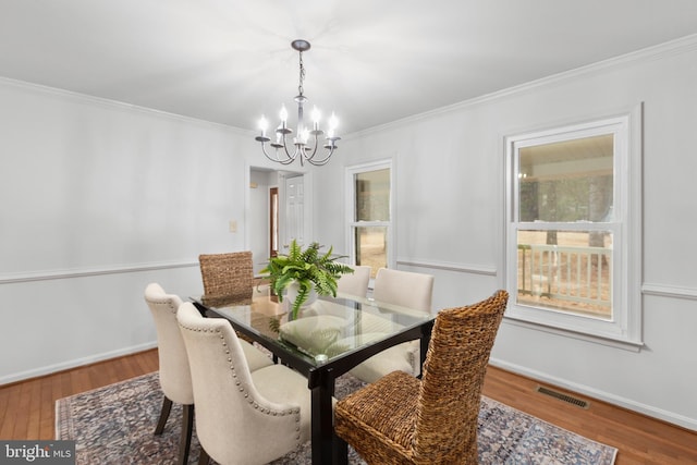 dining space with an inviting chandelier, visible vents, wood finished floors, and ornamental molding