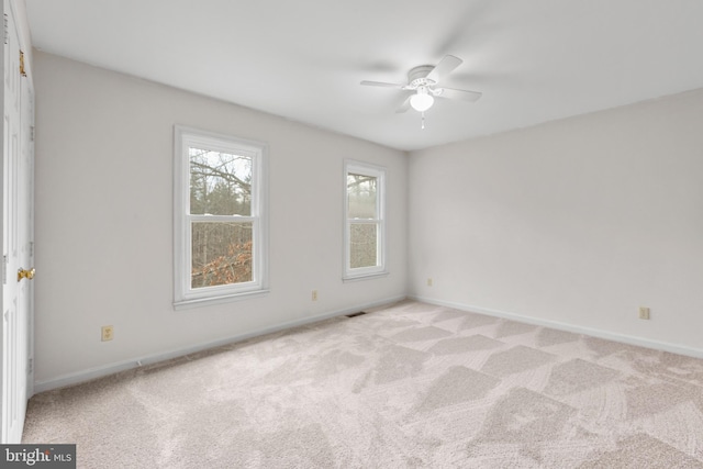 spare room with a ceiling fan, light colored carpet, visible vents, and baseboards