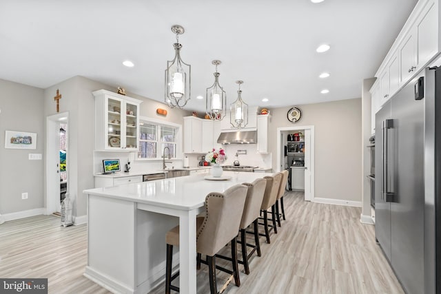 kitchen with a breakfast bar, stainless steel appliances, light countertops, white cabinets, and under cabinet range hood