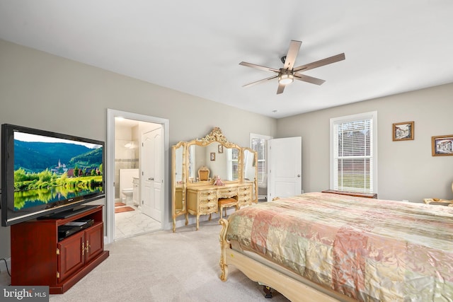 bedroom with ceiling fan, light colored carpet, and ensuite bath