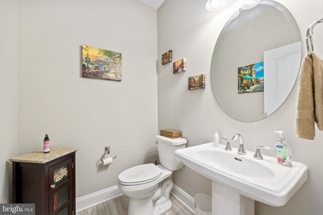 half bathroom featuring toilet, wood finished floors, baseboards, and a sink