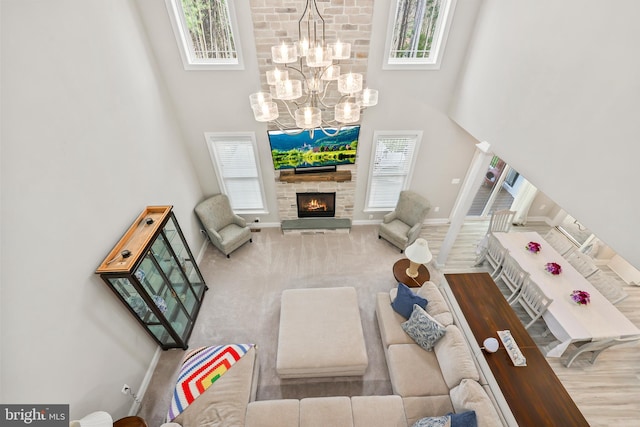 living room featuring a stone fireplace, an inviting chandelier, a high ceiling, and plenty of natural light