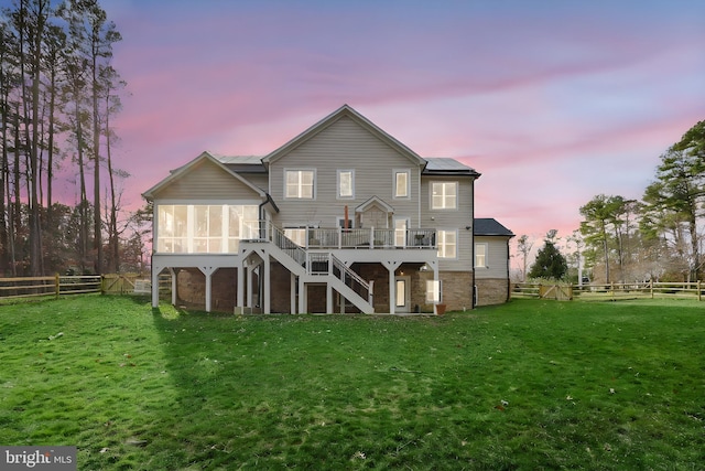 back of property at dusk with stairway, a lawn, a fenced backyard, and a sunroom