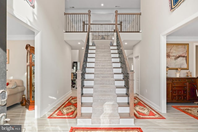 staircase with a high ceiling, wood finished floors, baseboards, and ornamental molding