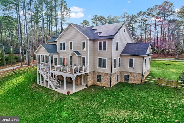 back of property with roof with shingles, a wooden deck, a yard, a patio area, and roof mounted solar panels