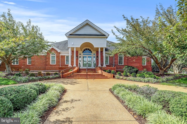 neoclassical home featuring french doors, brick siding, and driveway