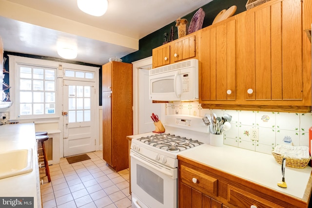 kitchen with brown cabinets, light tile patterned floors, light countertops, backsplash, and white appliances