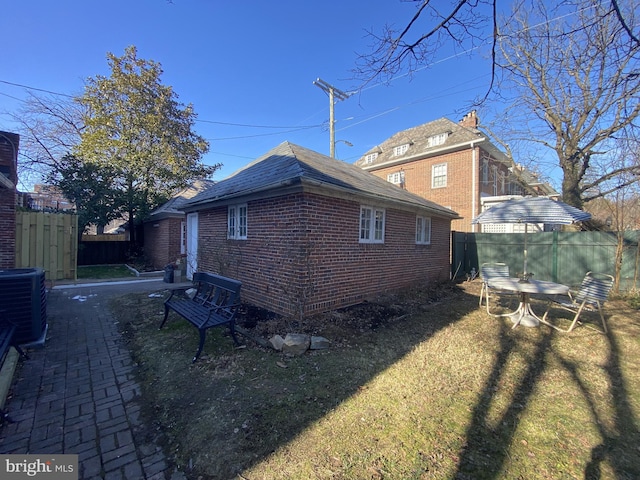 view of home's exterior with brick siding, fence, central AC unit, and a lawn