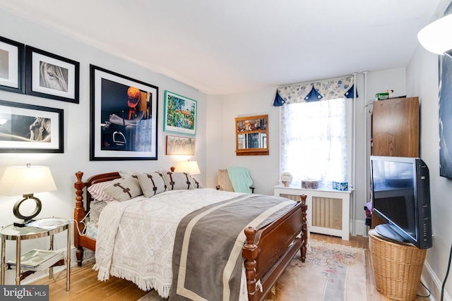 bedroom with radiator, light wood finished floors, and baseboards