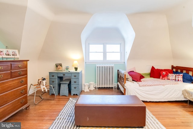 bedroom with vaulted ceiling, wood finished floors, and radiator