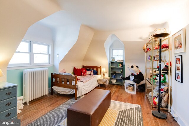 bedroom with multiple windows, wood finished floors, and radiator