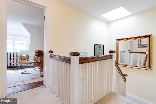 hallway with radiator heating unit, a skylight, wood finished floors, and an upstairs landing