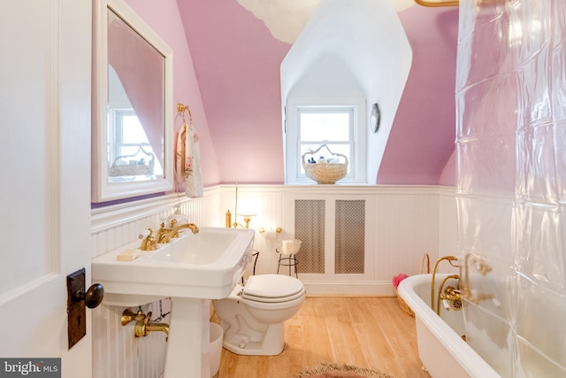 full bath featuring a tub to relax in, a wainscoted wall, toilet, and wood finished floors