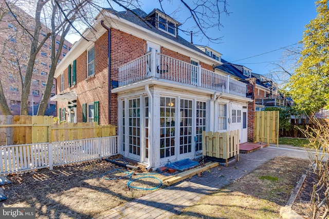 rear view of house with brick siding, fence, and a balcony