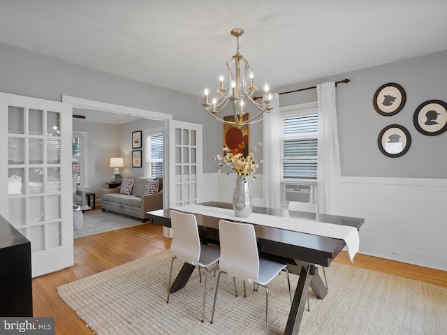 dining room with a wainscoted wall, a chandelier, cooling unit, and light wood-style floors