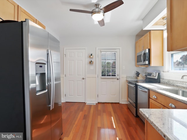 kitchen featuring a ceiling fan, appliances with stainless steel finishes, hardwood / wood-style floors, light stone countertops, and a sink