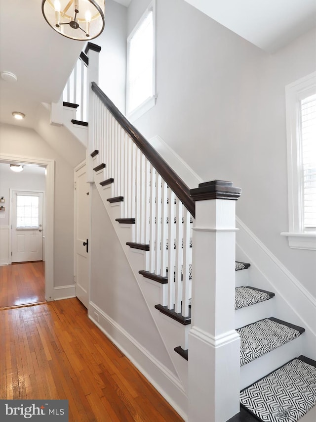 stairway with wood-type flooring, a high ceiling, baseboards, and an inviting chandelier