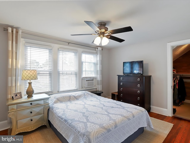 bedroom featuring cooling unit, wood finished floors, a ceiling fan, baseboards, and a walk in closet