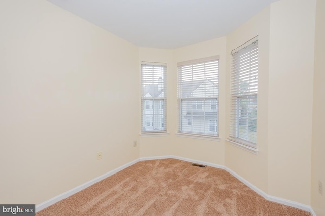 spare room featuring light carpet, visible vents, and baseboards