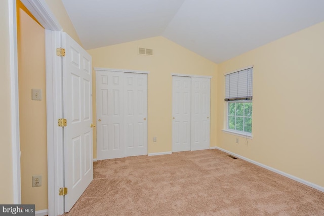 unfurnished bedroom with vaulted ceiling, light colored carpet, visible vents, and multiple closets