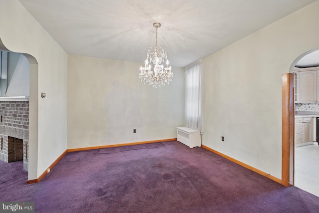 carpeted spare room featuring arched walkways, a brick fireplace, and baseboards