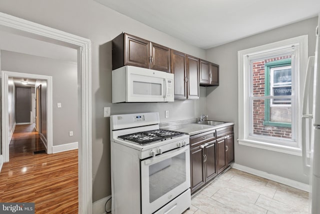 kitchen featuring white appliances, baseboards, a sink, and dark brown cabinets