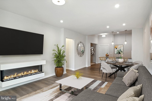 living area featuring baseboards, dark wood finished floors, a glass covered fireplace, and recessed lighting