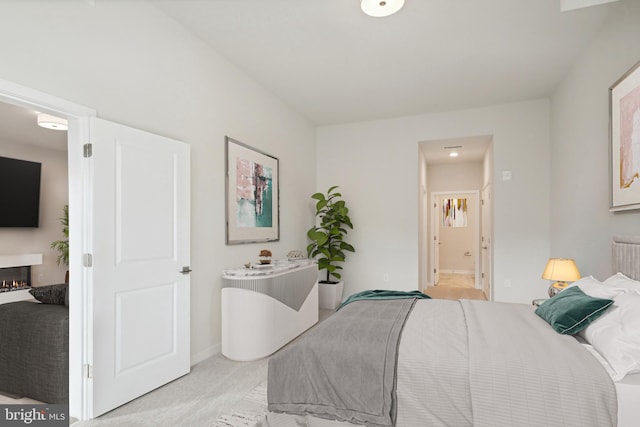 bedroom with a lit fireplace, baseboards, connected bathroom, and light colored carpet