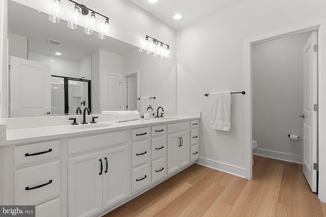 full bathroom with double vanity, visible vents, a sink, a shower stall, and wood finished floors