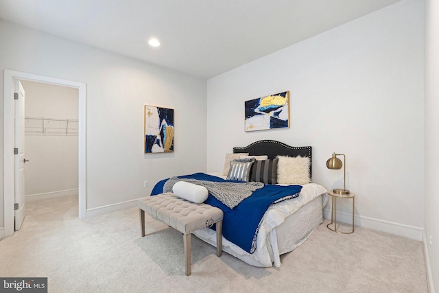 bedroom featuring light carpet, a walk in closet, and baseboards