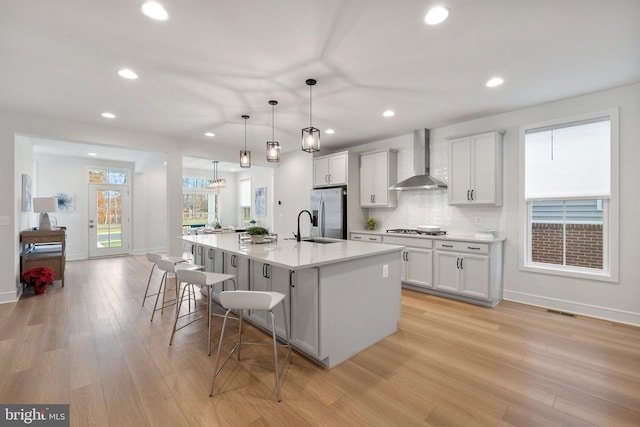 kitchen featuring a spacious island, wall chimney exhaust hood, decorative light fixtures, stainless steel appliances, and light countertops