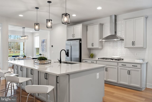 kitchen featuring a kitchen breakfast bar, a kitchen island with sink, stainless steel appliances, wall chimney range hood, and pendant lighting