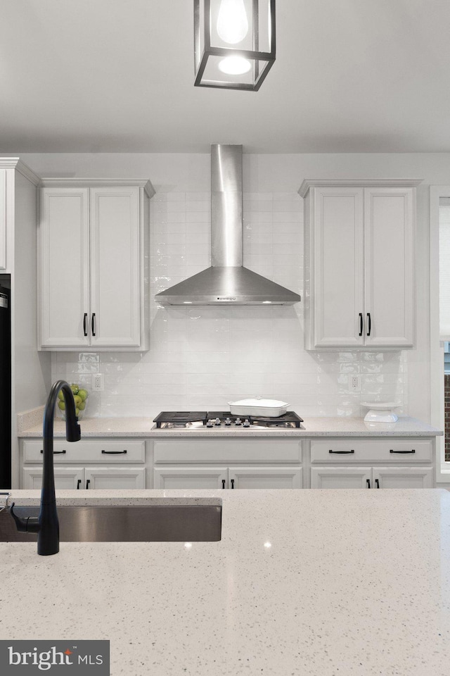 kitchen with tasteful backsplash, wall chimney exhaust hood, stainless steel gas cooktop, and white cabinets