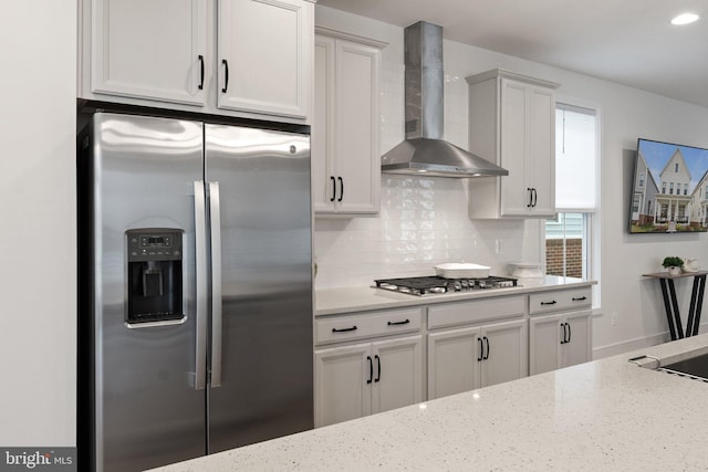 kitchen featuring light stone countertops, wall chimney exhaust hood, appliances with stainless steel finishes, and tasteful backsplash