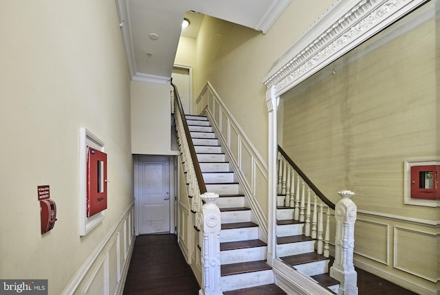 staircase featuring a high ceiling, a decorative wall, crown molding, and wood finished floors