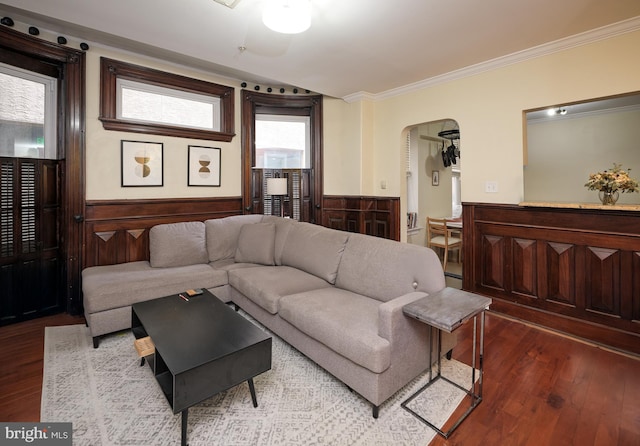 living room with arched walkways, wainscoting, wood finished floors, and crown molding