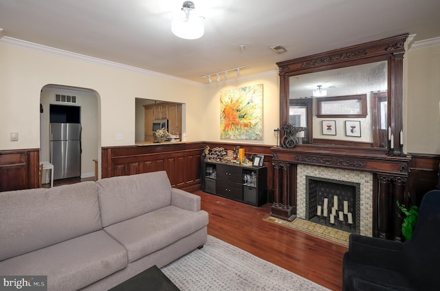 living room featuring arched walkways, a fireplace, wood finished floors, and crown molding