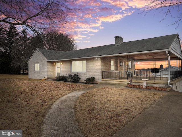 ranch-style home featuring covered porch, a shingled roof, a chimney, and brick siding