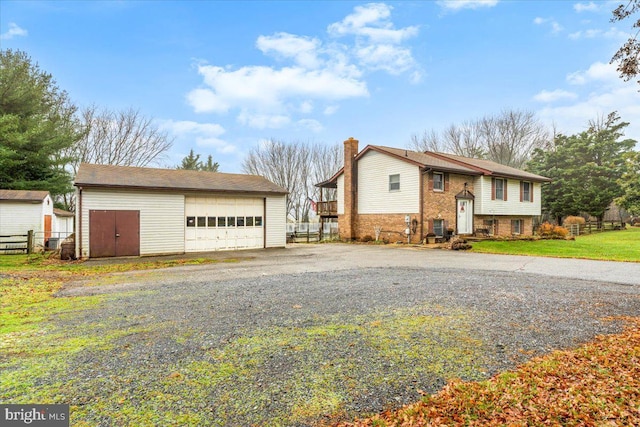 raised ranch with a chimney, a detached garage, an outbuilding, fence, and brick siding