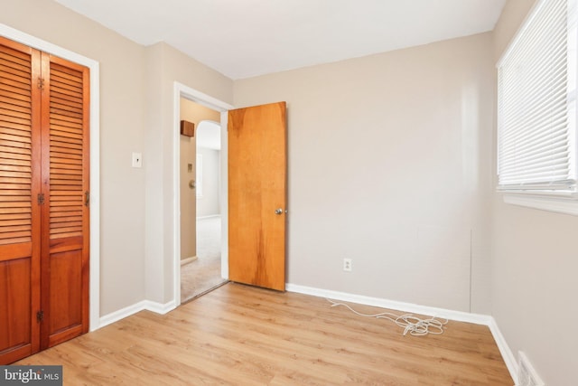 unfurnished bedroom with light wood-type flooring, baseboards, arched walkways, and a closet