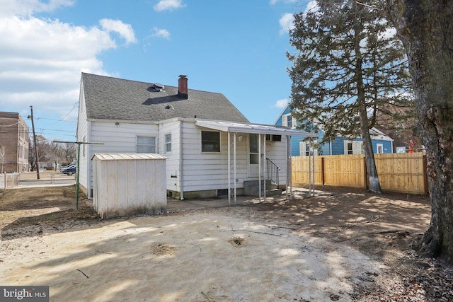 rear view of property featuring entry steps, roof with shingles, a chimney, and fence