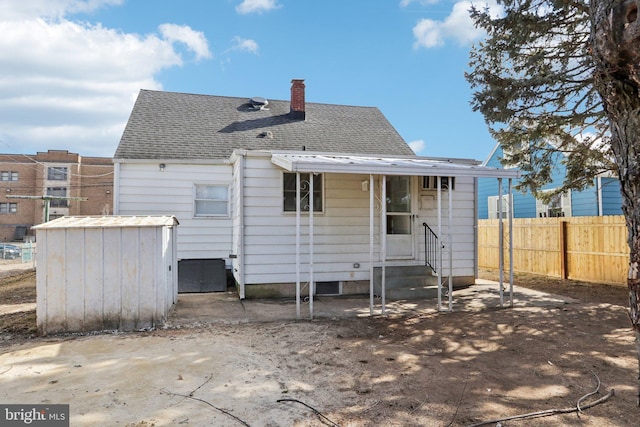 rear view of property featuring entry steps, roof with shingles, fence, and a chimney