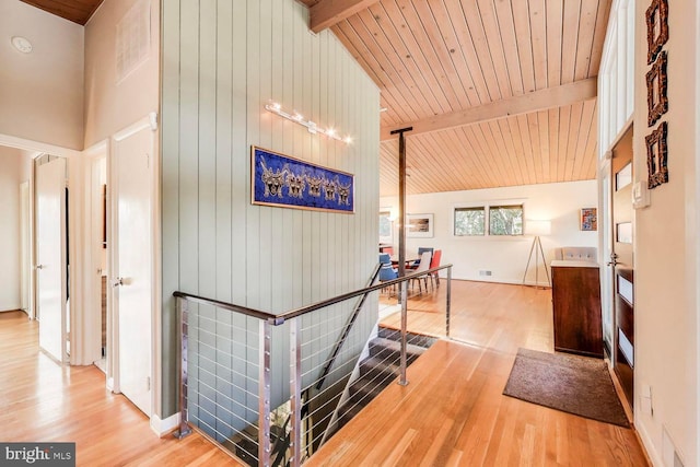 hallway with beam ceiling, wood finished floors, and an upstairs landing