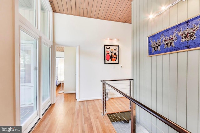 hall featuring wooden walls, wooden ceiling, light wood finished floors, and an upstairs landing