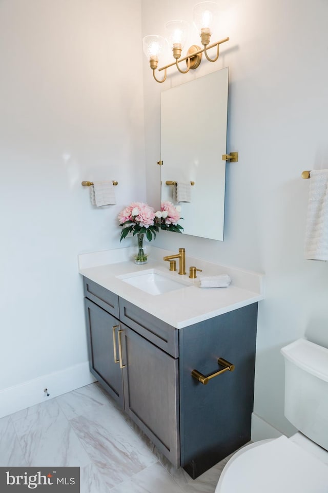 half bath featuring a chandelier, toilet, vanity, baseboards, and marble finish floor