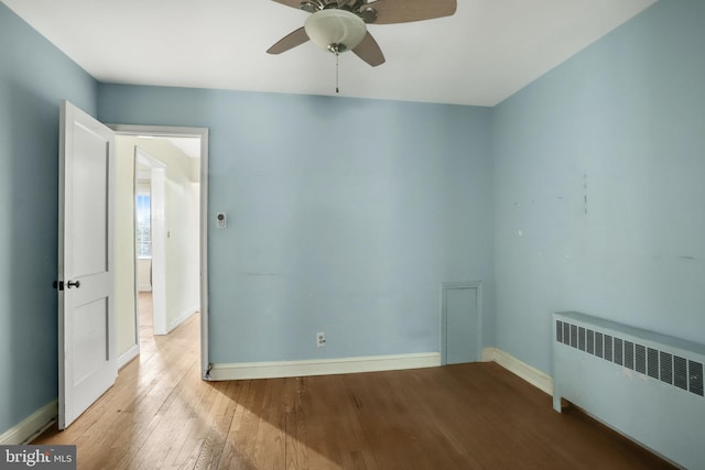 empty room with light wood finished floors, radiator heating unit, a ceiling fan, and baseboards