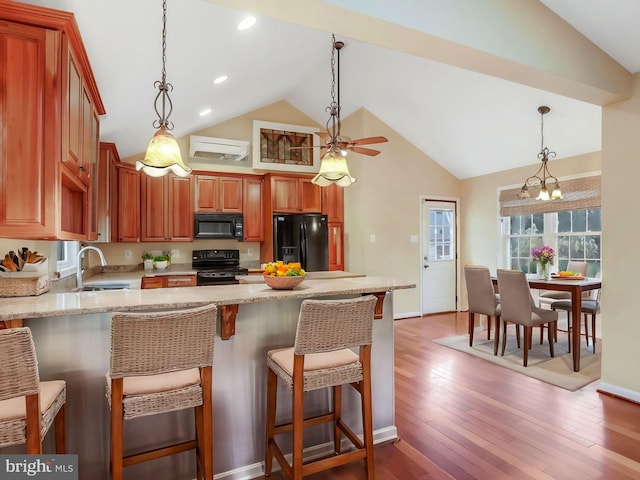 kitchen with decorative light fixtures, wood finished floors, black appliances, light stone countertops, and a kitchen breakfast bar