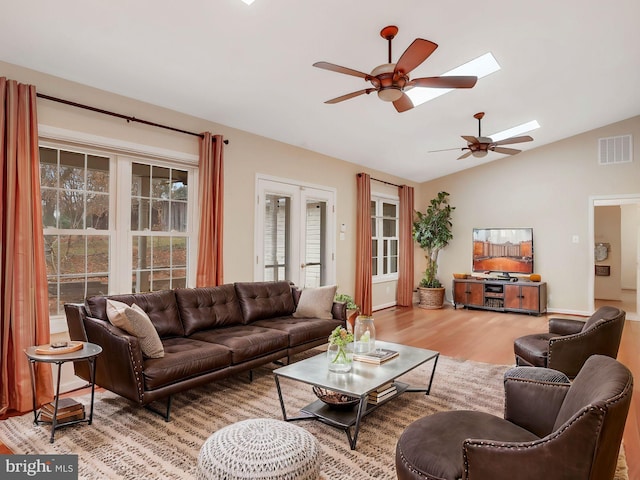 living room with a ceiling fan, vaulted ceiling with skylight, visible vents, and light wood-style flooring